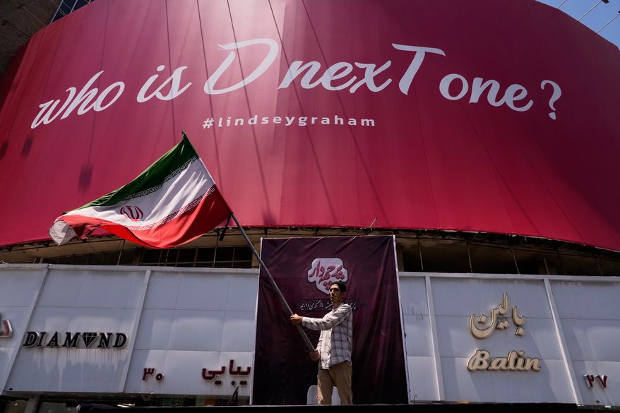 A man waves an Iranian flag beneath a billboard reading in English, "Who is D nexT one?" and "#lindseygraham," referring to late U.S. Sen. Lindsey Graham and using the capital letters "D" and "T" in an apparent play on the initials of U.S. President Donald Trump, in downtown Tehran, Iran, Thursday, July 16, 2026. (AP Photo/Vahid Salemi)