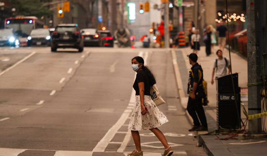 A woman wearing a mask crosses the street in Toronto as wildfire smoke fills the city, on Wednesday, July 15, 2026. (Laura Proctor/The Canadian Press via AP)