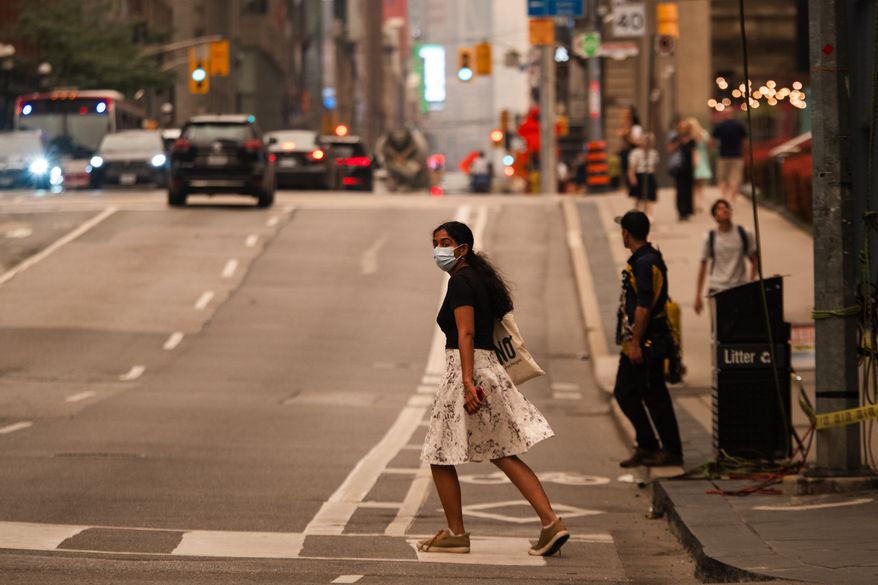 A woman wearing a mask crosses the street in Toronto as wildfire smoke fills the city, on Wednesday, July 15, 2026. (Laura Proctor/The Canadian Press via AP)