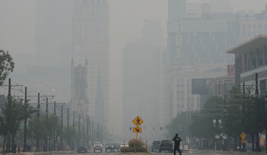 A pedestrian crosses the street as the Detroit city skyline is obscured during poor air quality due to smoke from Canadian wildfires Thursday, July 16, 2026, in Detroit. (AP Photo/Paul Sancya)