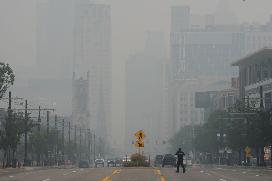 A pedestrian crosses the street as the Detroit city skyline is obscured during poor air quality due to smoke from Canadian wildfires Thursday, July 16, 2026, in Detroit. (AP Photo/Paul Sancya)