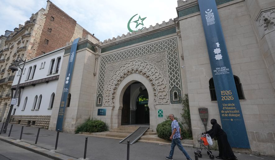 People walk past the Grand Mosque of Paris, where a banner reads, "100 years of light, a century of history, spirituality and dialogue" marking its 100th anniversary, Friday, July 17, 2026. (AP Photo/Michel Euler)