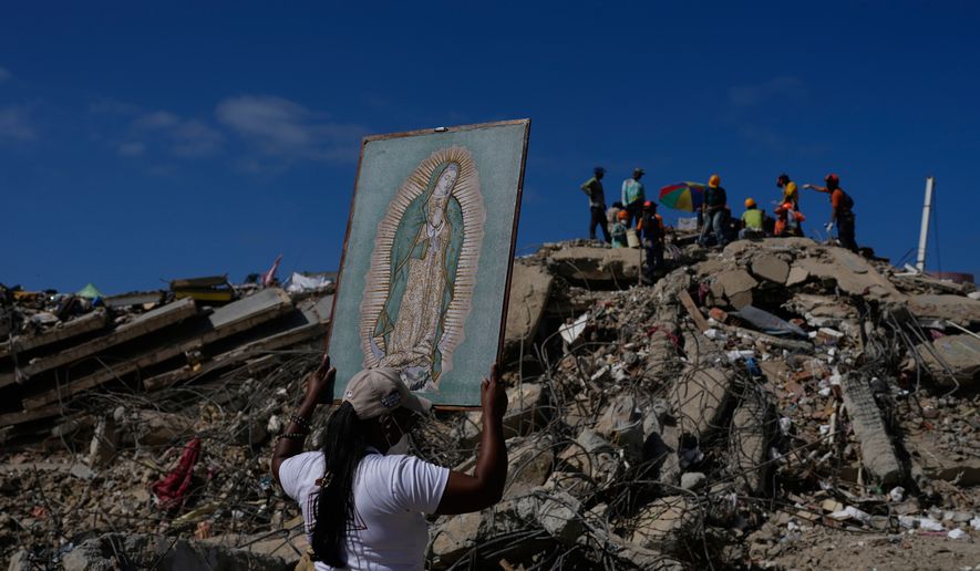 A woman holds a painting of the Virgin Mary as she accompanies a Catholic priest supporting people searching for the remains of relatives in the rubble of residential buildings that collapsed during the earthquakes that struck La Guaira, Venezuela, Friday, July 17, 2026. (AP Photo/Ariana Cubillos)