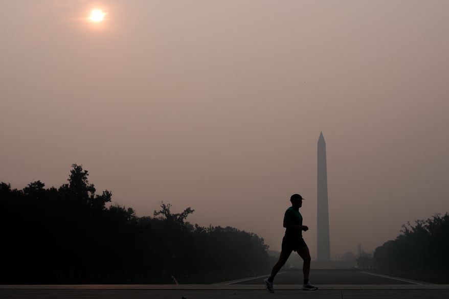 The sun is obscured by wildfire smoke as a person runs in front of the Washington Monument and Lincoln Memorial Reflecting Pool, Friday, July 17, 2026, on the National Mall in Washington. (AP Photo/Julia Demaree Nikhinson)