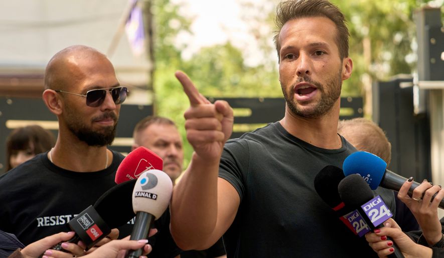 FILE - Andrew Tate, left, watches his brother Tristan speak, outside a police station in Voluntari, Romania, May 21, 2025. (AP Photo/Vadim Ghirda, File)