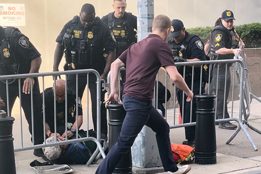 In this photo provided by Robert Sullivan several officers surround a person on the ground near the site of a fire at 26 Federal Plaza in lower Manhattan, Monday, July 20, 2026, in New York. (Robert Sullivan via AP)