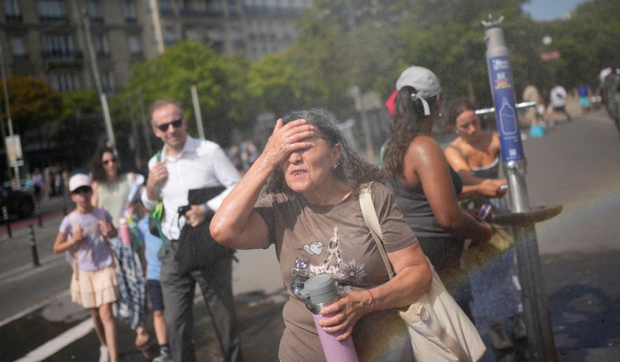 Tourists enjoy cooling off at a public water fountain In Paris, Friday, June 26, 2026. (AP Photo/Christophe Ena )