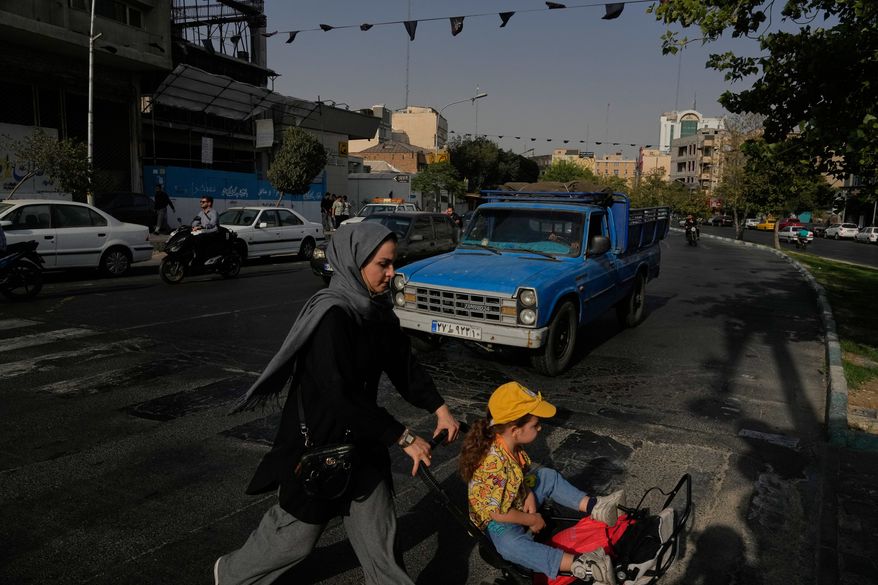 A woman crosses a street with a girl in downtown Tehran, Iran, Wednesday, July 22, 2026. (AP Photo/Vahid Salemi)