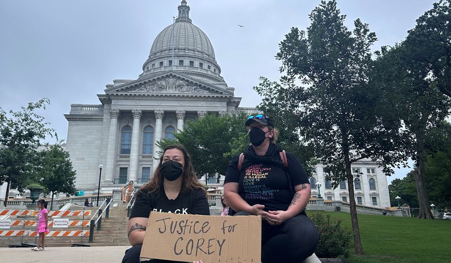 Lilly Nimmer, left, and Reba Bergmann, right, hold a sign to protest the police shooting of Corey Ruiz outside of the Wisconsin state Capitol during the weekly farmers market on Saturday, July 25, 2026, in Madison, Wisconsin. (AP Photo/Scott Bauer)