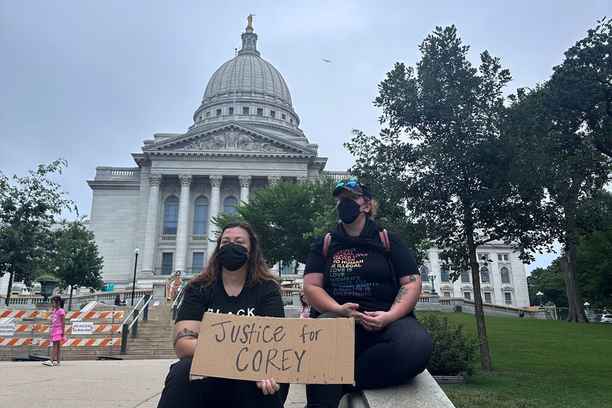 Lilly Nimmer, left, and Reba Bergmann, right, hold a sign to protest the police shooting of Corey Ruiz outside of the Wisconsin state Capitol during the weekly farmers market on Saturday, July 25, 2026, in Madison, Wisconsin. (AP Photo/Scott Bauer)