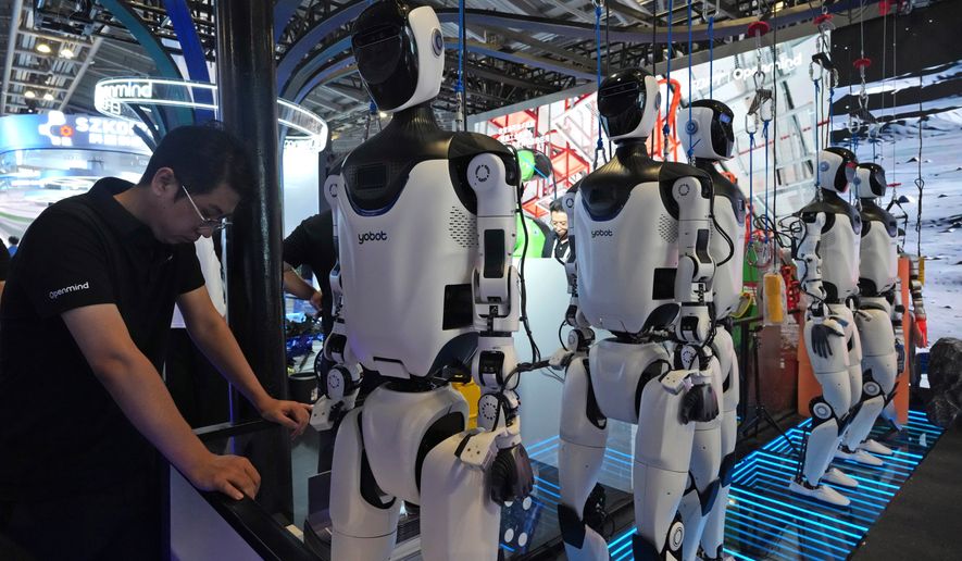 A worker reacts near a line of humanoid robots displayed at the World AI Conference in Shanghai, Friday, July 17, 2026. (AP Photo/Ng Han Guan)