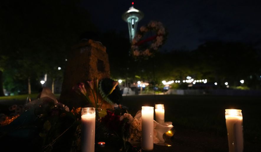 Flowers and candles are seen placed with the Space Needle at background, during the vigil for victims the day after a shooting at Seattle Center during the Bite of Seattle food festival, Monday, July 27, 2026, in Seattle. (AP Photo/Lindsey Wasson)