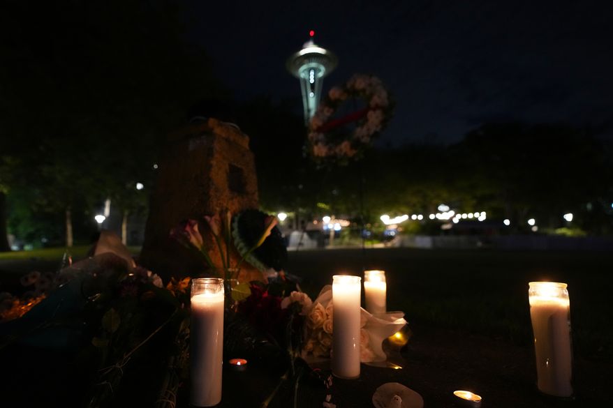 Flowers and candles are seen placed with the Space Needle at background, during the vigil for victims the day after a shooting at Seattle Center during the Bite of Seattle food festival, Monday, July 27, 2026, in Seattle. (AP Photo/Lindsey Wasson)