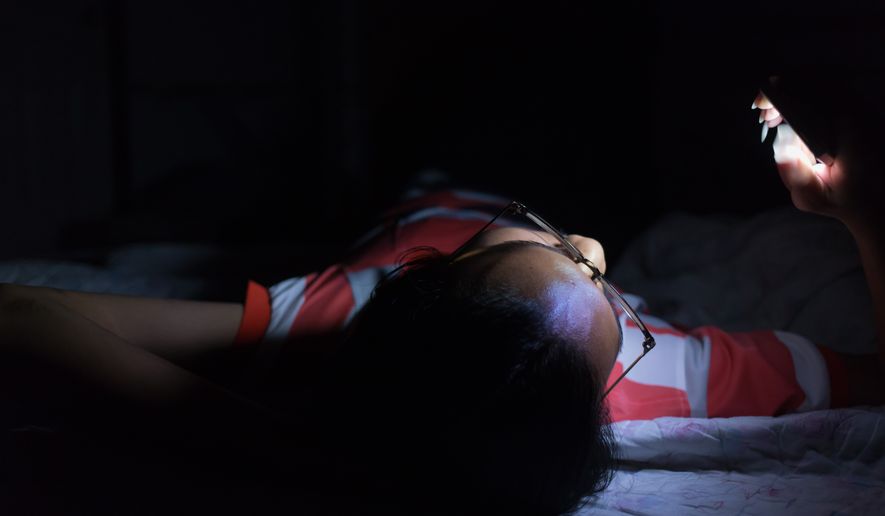 Young man using his smartphone on the bed in a dark room. File photo credit: Gap_Abstracture via Shutterstock