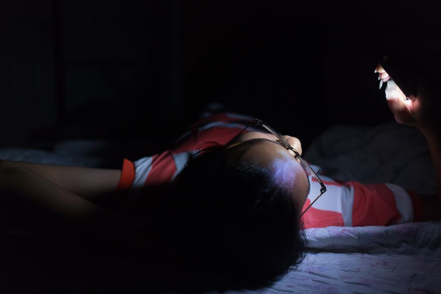 Young man using his smartphone on the bed in a dark room. File photo credit: Gap_Abstracture via Shutterstock