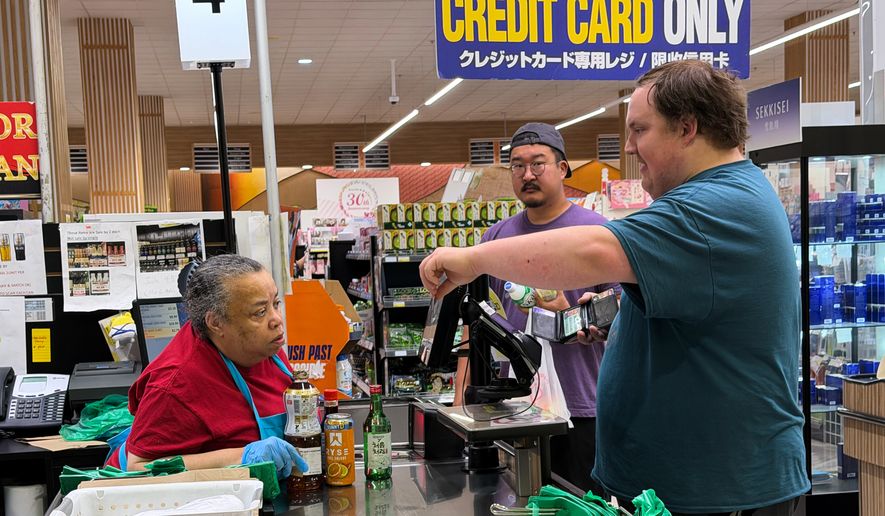 An employee checks a customer's identification card before checking out alcohol at a cash register in a grocery store in Arlington Heights, Ill., Monday, July 6, 2026. (AP Photo/Nam Y. Huh)