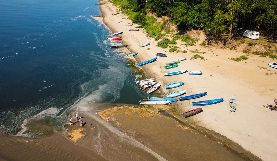 People stand on a bank of sand on the Danube River as usually submerged areas are exposed due to extreme low levels of the water following an extended period of drought in Corabia, Romania, Wednesday, July 29, 2026. (AP Photo/Nicolae Dumitrache)