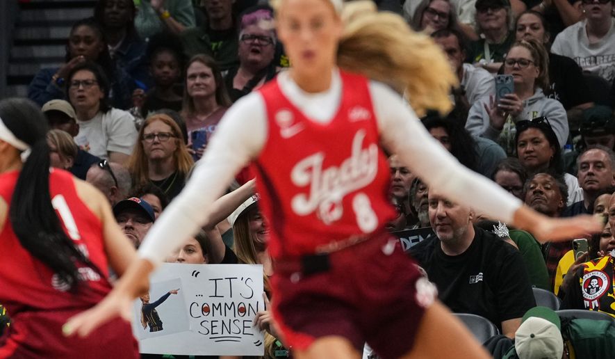 Indiana Fever guard Sophie Cunningham, front, runs by a fan holding a sign referencing her comments on transgender athletes and women's sports during the first half of a WNBA basketball game against the Seattle Storm, Tuesday, July 28, 2026, in Seattle. (AP Photo/Lindsey Wasson) **FILE**