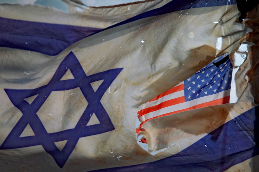 A U.S. flag is seen through a hole torn in an Israel national flag, as they wave in the wind at a horse ranch, near the southern Israeli town of Sderot, Friday, Nov. 20, 2020. (AP Photo/Oded Balilty, File)