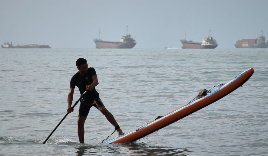 A man paddles a stand-up paddleboard as cargo ships and other commercial vessels appear anchored in the Strait of Hormuz off Bandar Abbas, Iran, Monday, July 27, 2026. (Razieh Poudat/ISNA via AP)