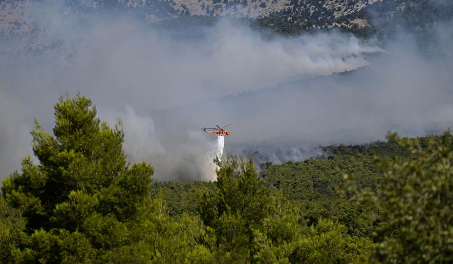 A firefighting helicopter drops water over a smoke-filled forest during a wildfire near Porto Germeno, northwest of Athens, Greece, Sunday, Aug. 2, 2026. (AP Photo/Michael Varaklas)