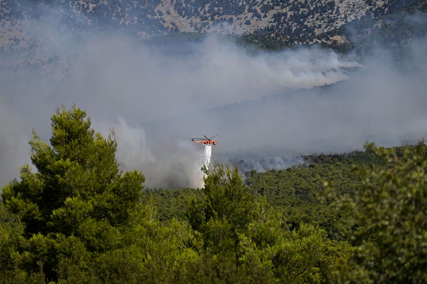 A firefighting helicopter drops water over a smoke-filled forest during a wildfire near Porto Germeno, northwest of Athens, Greece, Sunday, Aug. 2, 2026. (AP Photo/Michael Varaklas)