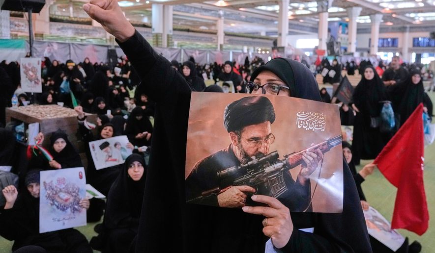 A mourner chants slogan as she holds a poster with graphic depicting Iran's Supreme Leader Ayatollah Mojtaba Khamenei in a ceremony commemorating the late Supreme Leader Ayatollah Ali Khamenei at the Imam Khomeini Mosalla Grand Mosque in Tehran, Tuesday, July 14, 2026. (AP Photo/Vahid Salemi)