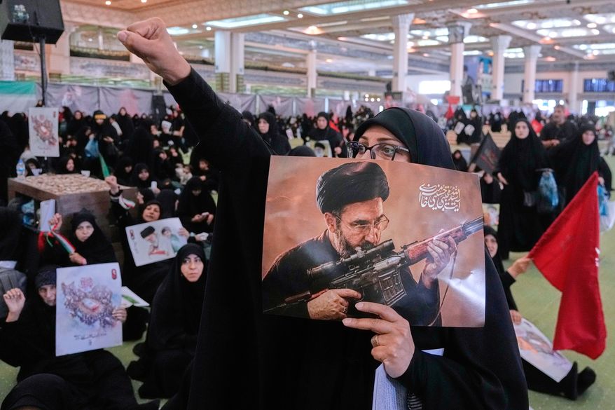A mourner chants slogan as she holds a poster with graphic depicting Iran's Supreme Leader Ayatollah Mojtaba Khamenei in a ceremony commemorating the late Supreme Leader Ayatollah Ali Khamenei at the Imam Khomeini Mosalla Grand Mosque in Tehran, Tuesday, July 14, 2026. (AP Photo/Vahid Salemi)