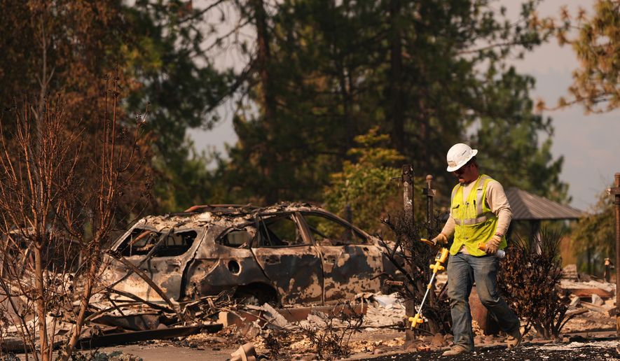 A worker with Avista moves through a property after a wildfire hit the northern part of Spokane, Wash., Monday, Aug. 3, 2026. (AP Photo/Lindsey Wasson)