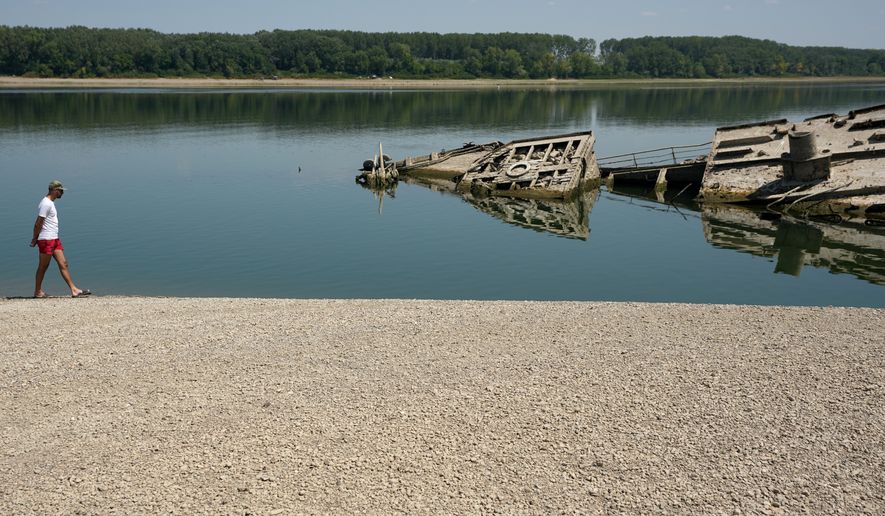 A man walks on the sandbank by the wreckage of a WWII German warship, emerged due to the drought, in front of Djerdap II, a large dam on the Danube River, between Romania and Serbia, near Prahovo, Serbia, Tuesday, Aug. 4, 2026. (AP Photo/Darko Vojinovic)