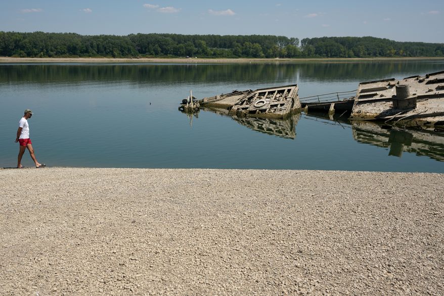 A man walks on the sandbank by the wreckage of a WWII German warship, emerged due to the drought, in front of Djerdap II, a large dam on the Danube River, between Romania and Serbia, near Prahovo, Serbia, Tuesday, Aug. 4, 2026. (AP Photo/Darko Vojinovic)