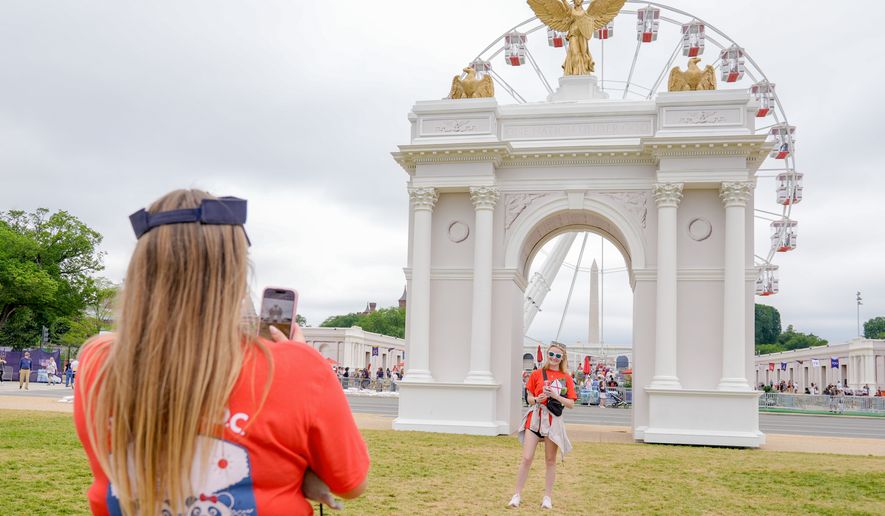 Visitors take photos at the Great American State Fair on the National Mall, with the ferris wheel and a model of the triumphal arch in the background, Thursday, July 9, 2026, in Washington. (AP Photo/Mariam Zuhaib)