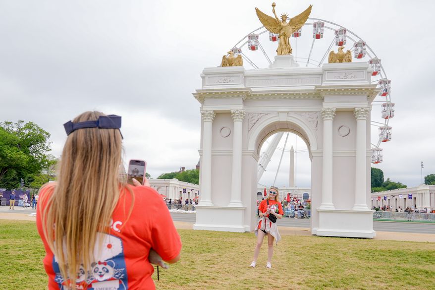Visitors take photos at the Great American State Fair on the National Mall, with the ferris wheel and a model of the triumphal arch in the background, Thursday, July 9, 2026, in Washington. (AP Photo/Mariam Zuhaib)
