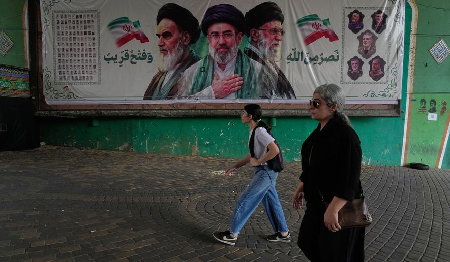 Women walk past a banner showing portraits of the late Iranian revolutionary founder Ayatollah Khomeini, left, Supreme Leader Ayatollah Mojtaba Khamenei, center, and the late Supreme Leader Ayatollah Ali Khamenei, who was killed in the U.S. and Israel strike on Feb. 28, under a bridge in northern Tehran, Iran, Sunday, Aug. 2, 2026. (AP Photo/Vahid Salemi)