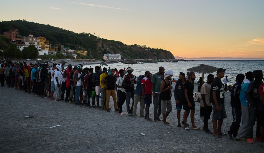 Migrants who crossed from Morocco into Spain line up for food distribution on a beach in the Spanish enclave of Ceuta, Monday, Aug. 3, 2026. (AP Photo/Bernat Armangue)