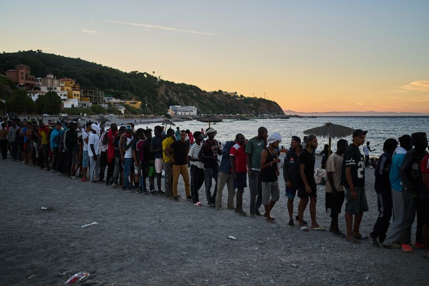 Migrants who crossed from Morocco into Spain line up for food distribution on a beach in the Spanish enclave of Ceuta, Monday, Aug. 3, 2026. (AP Photo/Bernat Armangue)