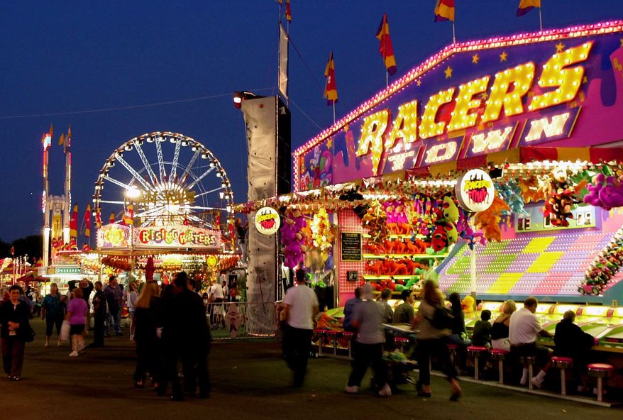 With a ferris wheel in the background fair goers pass by brightly-lit attractions at the Orange County Fairgrounds Wednesday, July 18, 2001, in Costa Mesa, Calif. (AP Photo/Kevork Djansezian)