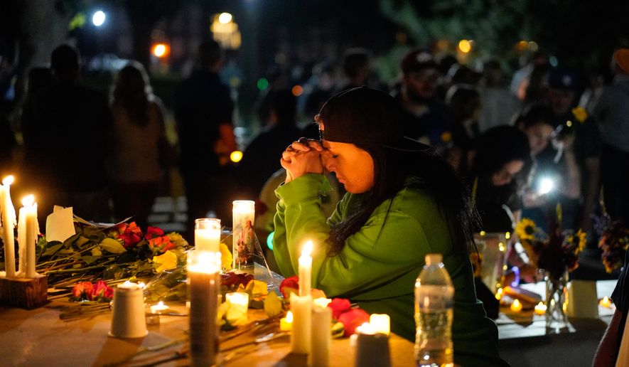 A woman prays during a candlelight vigil Tuesday, Aug. 4, 2026, in Twin Falls, Idaho, to honor the victims of a recent shooting at a local In-N-Out Burger. (AP Photo/Andrew Eakin)
