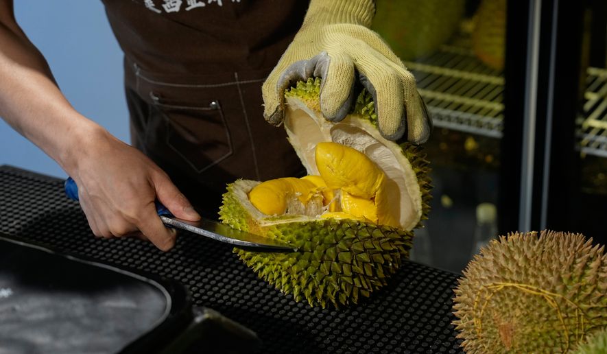 A worker opens durian fruits imported from Malaysia to pack and deliver for customer at a shop in Beijing, China, Monday, July 13, 2026. (AP Photo/Andy Wong)