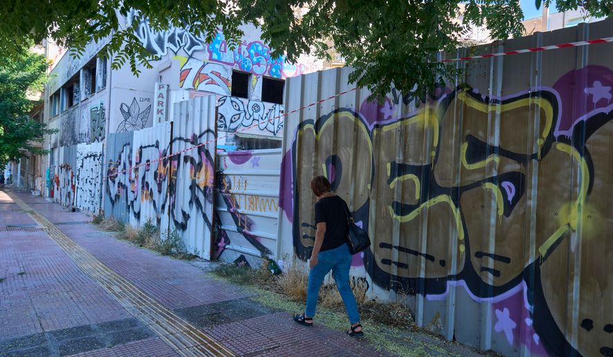 A woman walks past the abandoned building where the body of Scottish woman Elisabeth Jane Ross was found inside a suitcase in Athens, Greece, Wednesday, Aug. 5, 2026. (AP Photo/Petros Giannakouris)