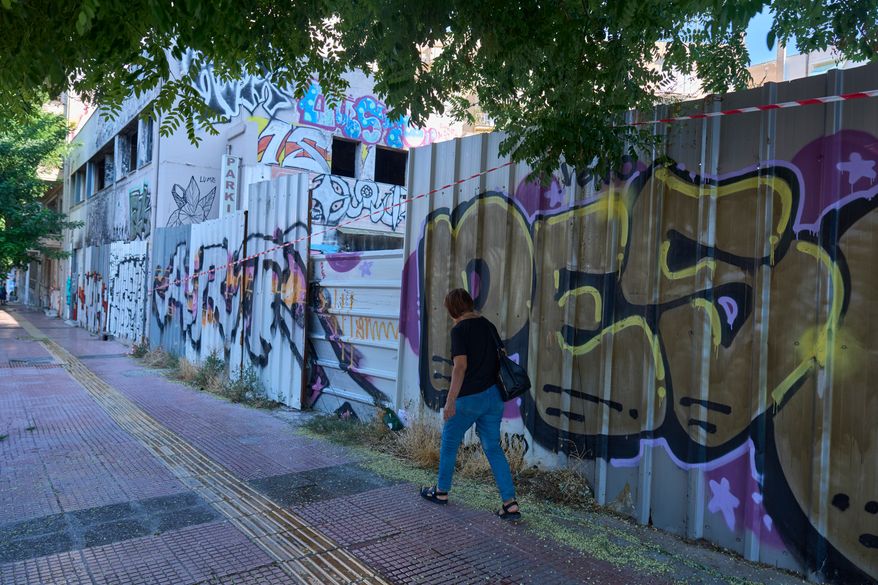 A woman walks past the abandoned building where the body of Scottish woman Elisabeth Jane Ross was found inside a suitcase in Athens, Greece, Wednesday, Aug. 5, 2026. (AP Photo/Petros Giannakouris)
