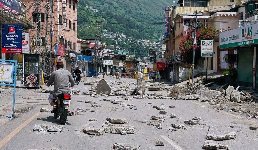Motorcyclists navigate through a road barricaded with concrete blocks set up by supporters of the outlawed Joint Awami Action Committee (JAAC) during a protest demanding greater political rights and the abolition of 12 legislative refugee seats, in Muzaffarabad, the capital of Pakistan-administered Kashmir, Saturday, Aug. 1, 2026 (AP Photo/M.D. Mughal)