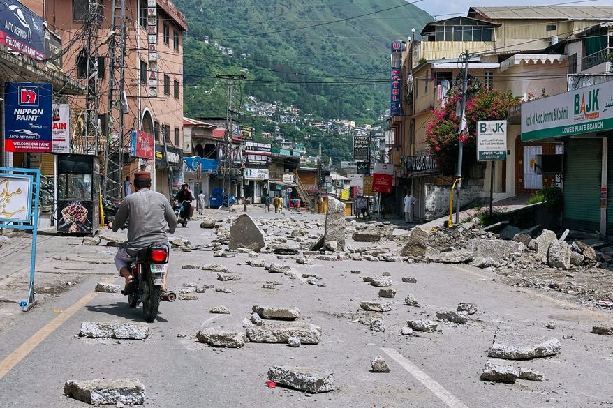 Motorcyclists navigate through a road barricaded with concrete blocks set up by supporters of the outlawed Joint Awami Action Committee (JAAC) during a protest demanding greater political rights and the abolition of 12 legislative refugee seats, in Muzaffarabad, the capital of Pakistan-administered Kashmir, Saturday, Aug. 1, 2026 (AP Photo/M.D. Mughal)