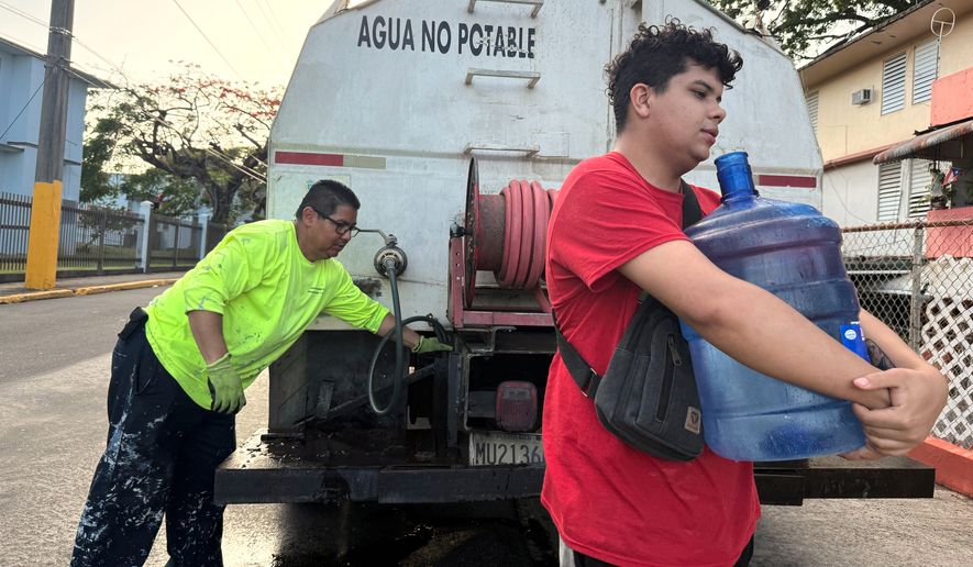 FILE - Bryan Pérez hauls a five-gallon water jug to his apartment in the Villa Kennedy public housing complex in San Juan, Puerto Rico, June 10, 2026. (AP Photo/Danica Coto, File)