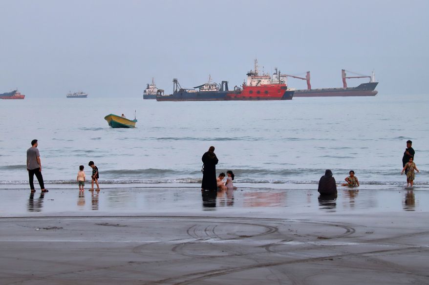 People spend time at a beach as commercial vessels are anchored in the Strait of Hormuz off Bandar Abbas, Iran, Wednesday, Aug. 5, 2026. (Amirhosein Khorgooi/ISNA via AP)