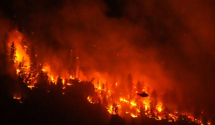 FILE - A helicopter conducting night operations prepares to drop water on the Quilpituk Creek wildfire burning on the west side of Okanagan Lake near Fintry, British Columbia, Aug. 3, 2026. (Darryl Dyck/The Canadian Press via AP, File)