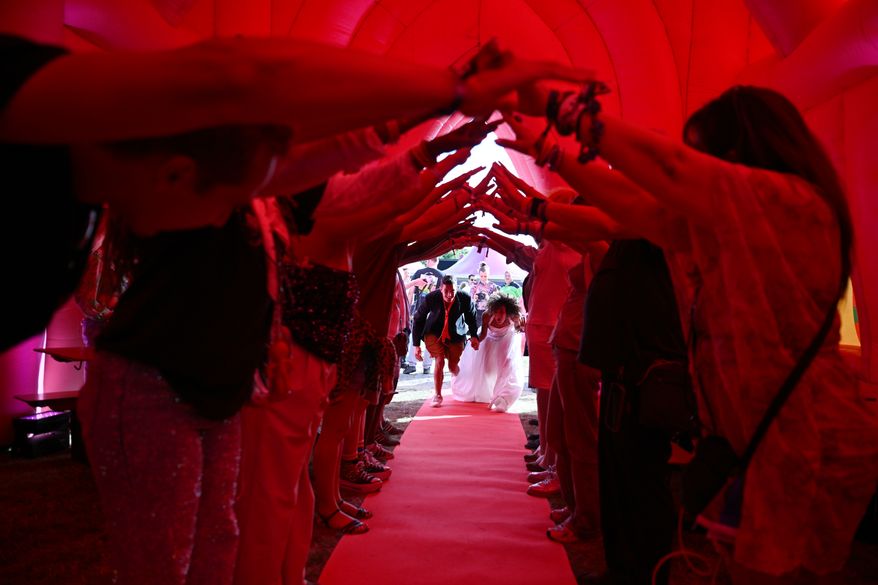 Guests create a human arch for a couple as they enter an inflatable chapel during a mass wedding ceremony in Amsterdam, Netherlands, Thursday, Aug. 6, 2026, as part of Pride events celebrating 25 years since the Netherlands became the first country in the world to legalize same-sex marriage. (AP Photo/Mouneb Taim)