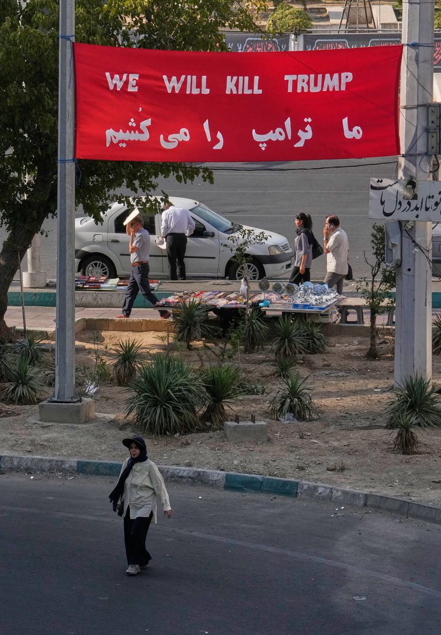 A woman walks beneath a banner reading in English and Farsi, "We will kill Trump," at a square in Tehran, Iran, Monday, Aug. 10, 2026. (AP Photo/Vahid Salemi)