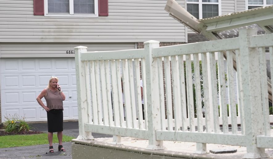 Kerry Hourigan speaks on the phone after reviewing damage a storm caused to her home in Tinley Park, Ill., Tuesday, Aug. 11, 2026. (AP Photo/Laura Bargfeld)