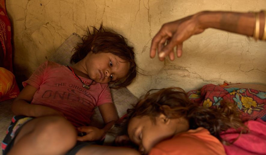 Sonam Mukhiya, left, lies next to her 3-year-old brother, Yubraj Mukhiya, and their grandmother in their home in Gaur, Nepal, on May 19, 2026. Their mother, Kabita Mukhiya, died in December while 28-weeks pregnant amid disruptions to nutrition programs and reproductive outreach services following last year's foreign aid cuts by the United States. (AP Photo/Bram Janssen)